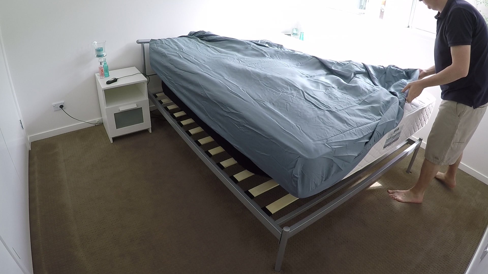 Queen mattress being held at working height by Bedezy, person mid way through putting on a fitted sheet with both hands in and body in an upright position.